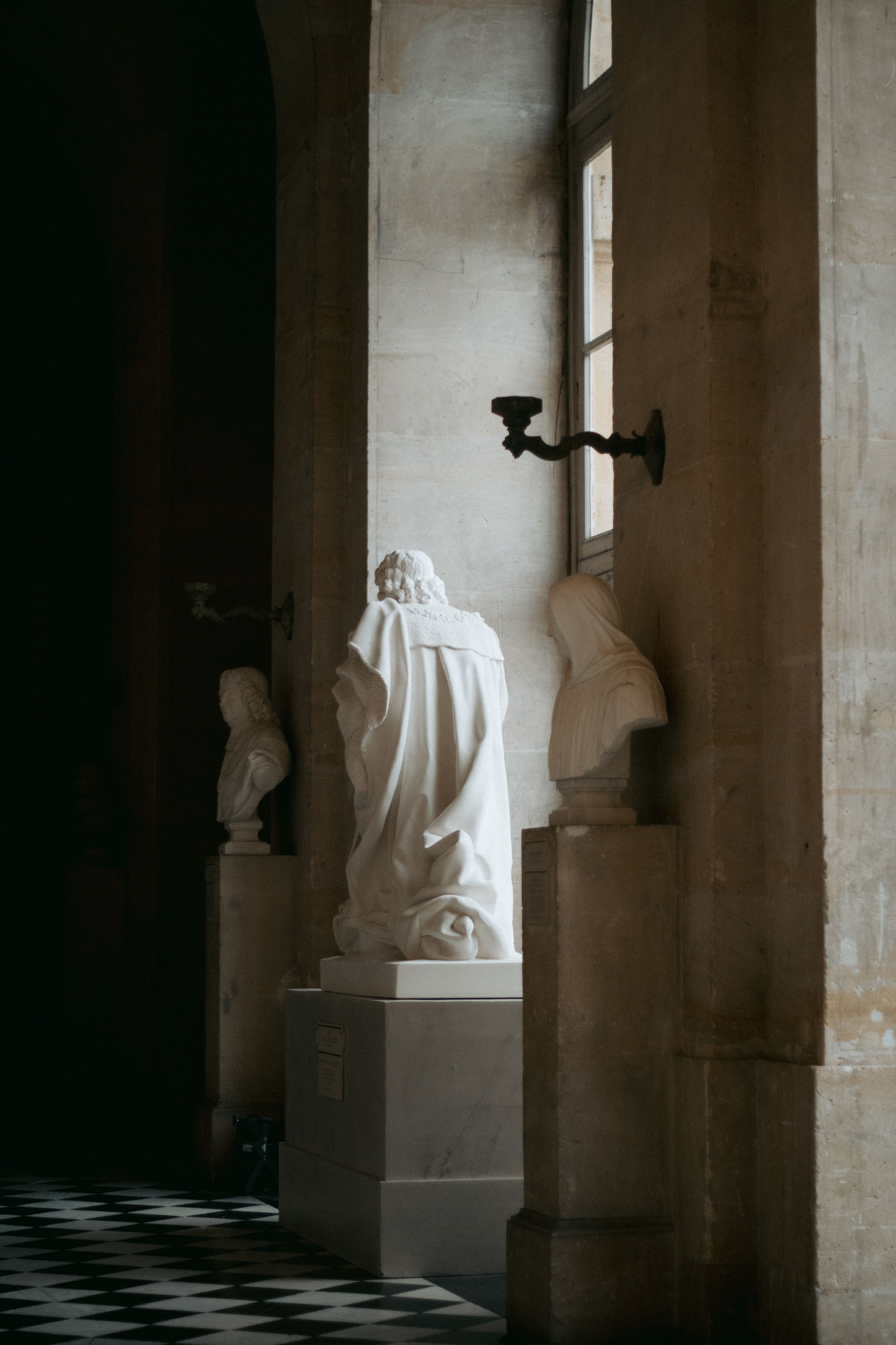 Elegant statues illuminated by sunlight in the hallway of Versailles Palace, France.