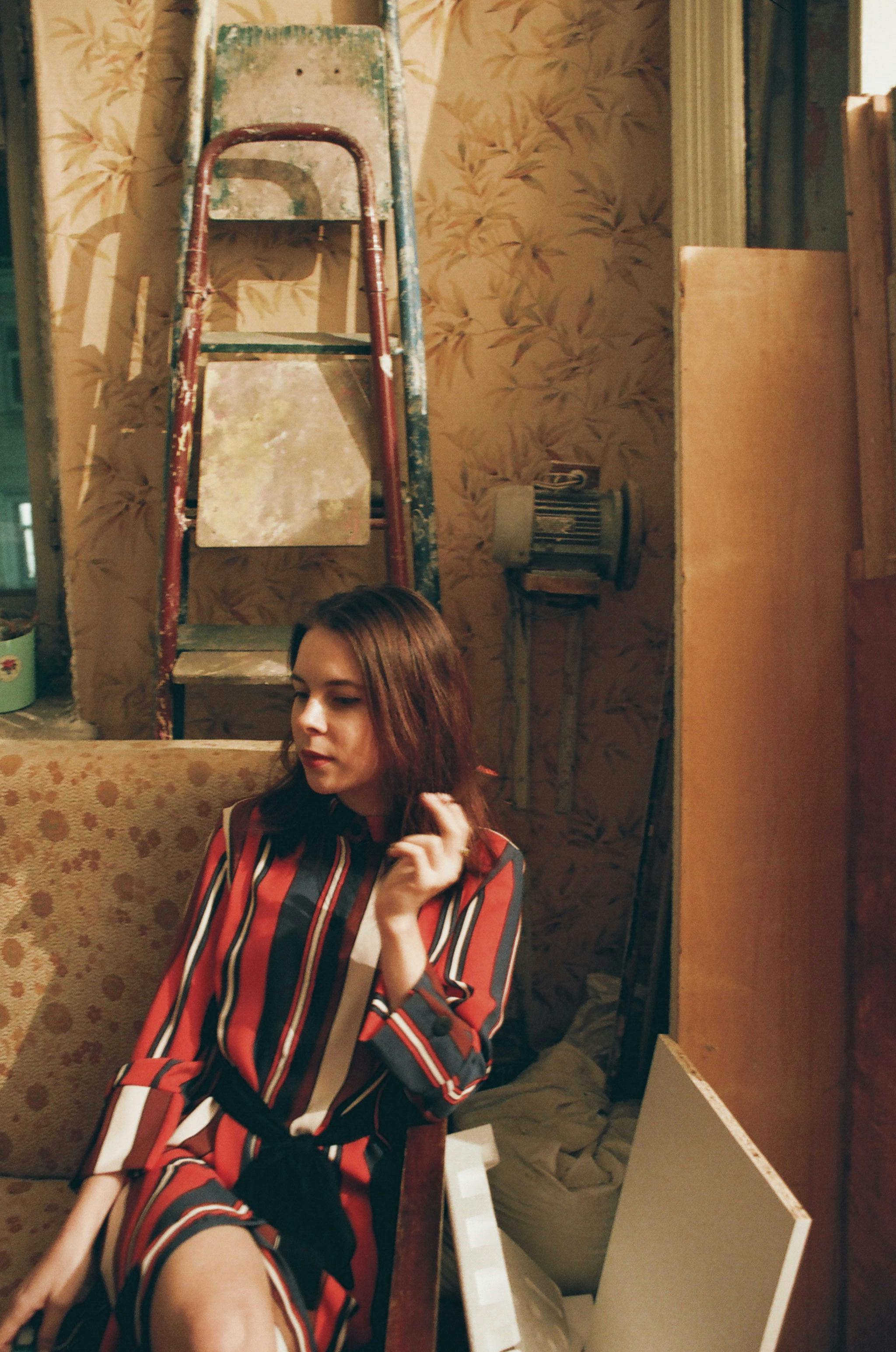 一位时尚女士身穿红色连衣裙，坐在室内的复古梯子旁，散发着别致的气息