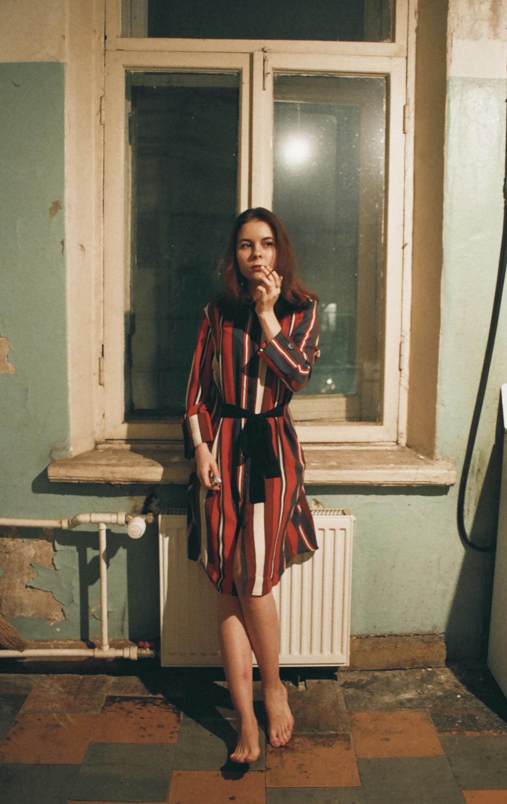 woman wearing red white and black striped long sleeved flare dress standing beside window pane