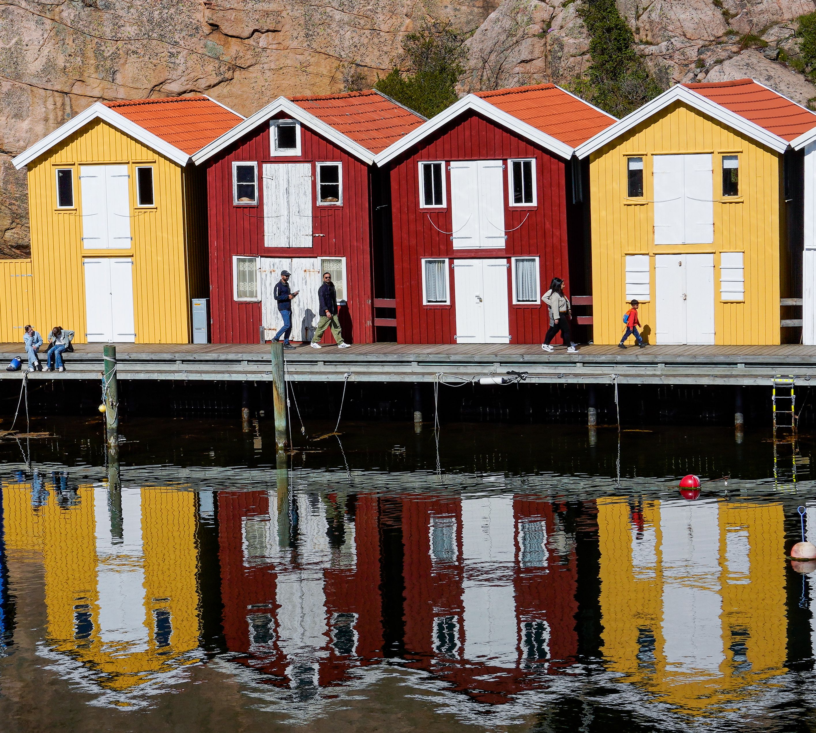 Vibrant Nordic architecture in Smögen reflecting on calm waters with people strolling by.