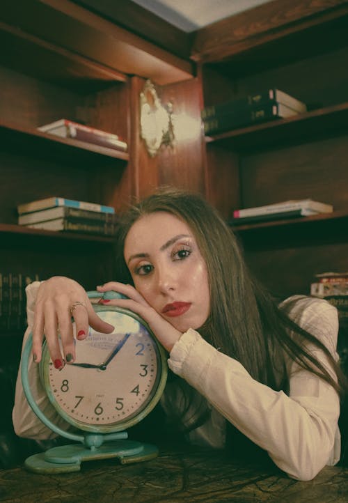 A woman holding an old clock in front of her face