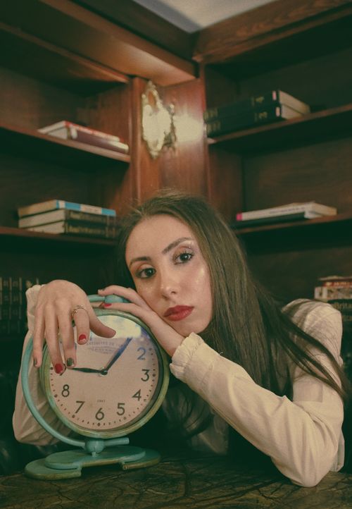 Free A contemplative woman rests against a vintage clock in a cozy library setting. Stock Photo