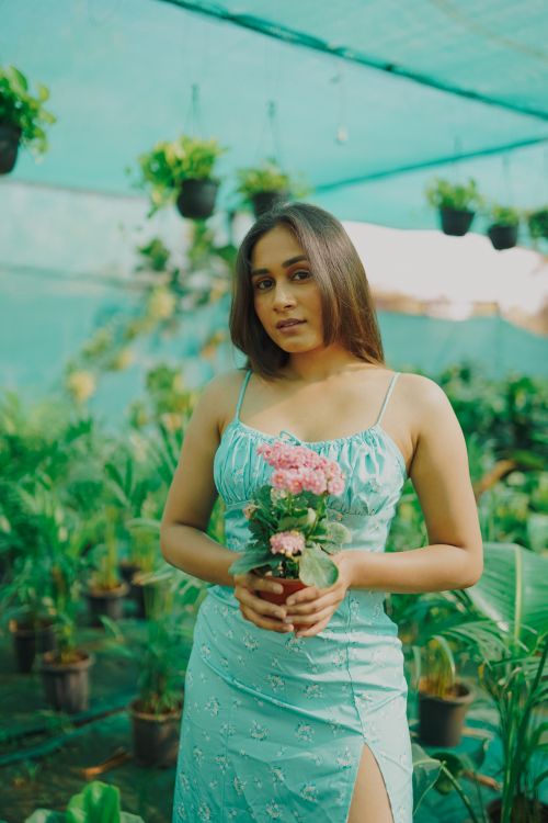 Free Young woman in a dress holding a flower pot in a vibrant greenhouse. Stock Photo