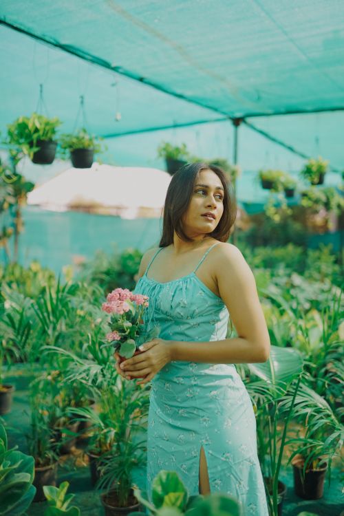 Free A woman in a blue dress holding flowers in a lush greenhouse setting. Stock Photo