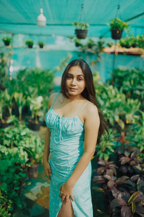 Free Portrait of a woman in a green dress standing in a lush greenhouse garden. Stock Photo