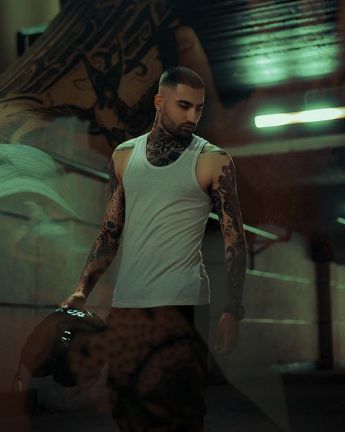 Free Artistic photo of tattooed man in a white tank top holding a helmet in an industrial setting. Stock Photo