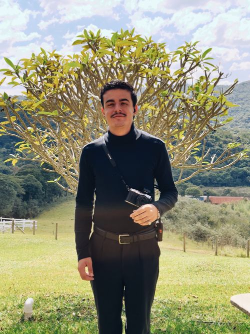 Free Smiling man in black clothes with camera, posing in a sunny outdoor setting with a tree in the background. Stock Photo