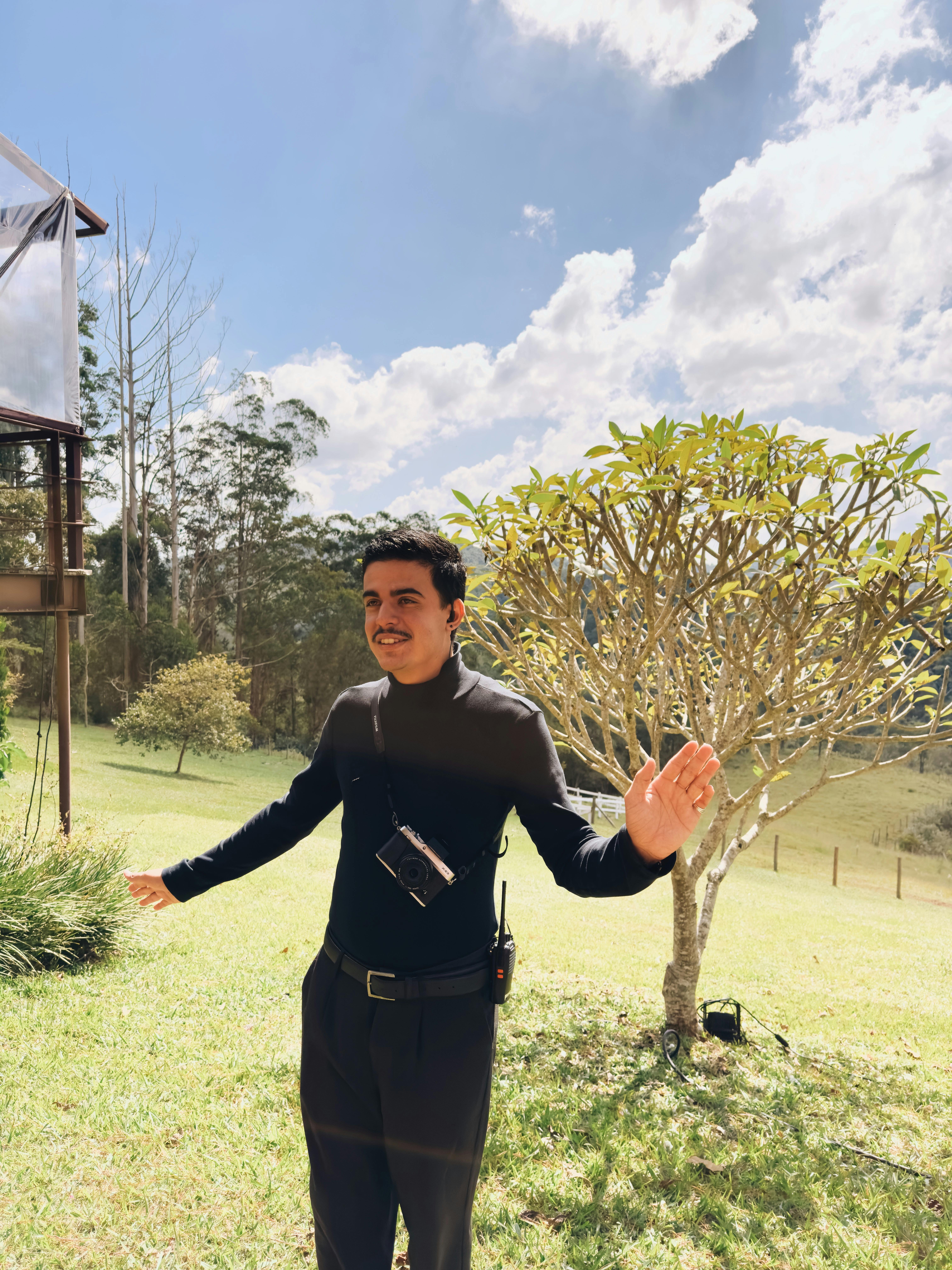 Man with camera posing outdoors in sunny rural setting with trees