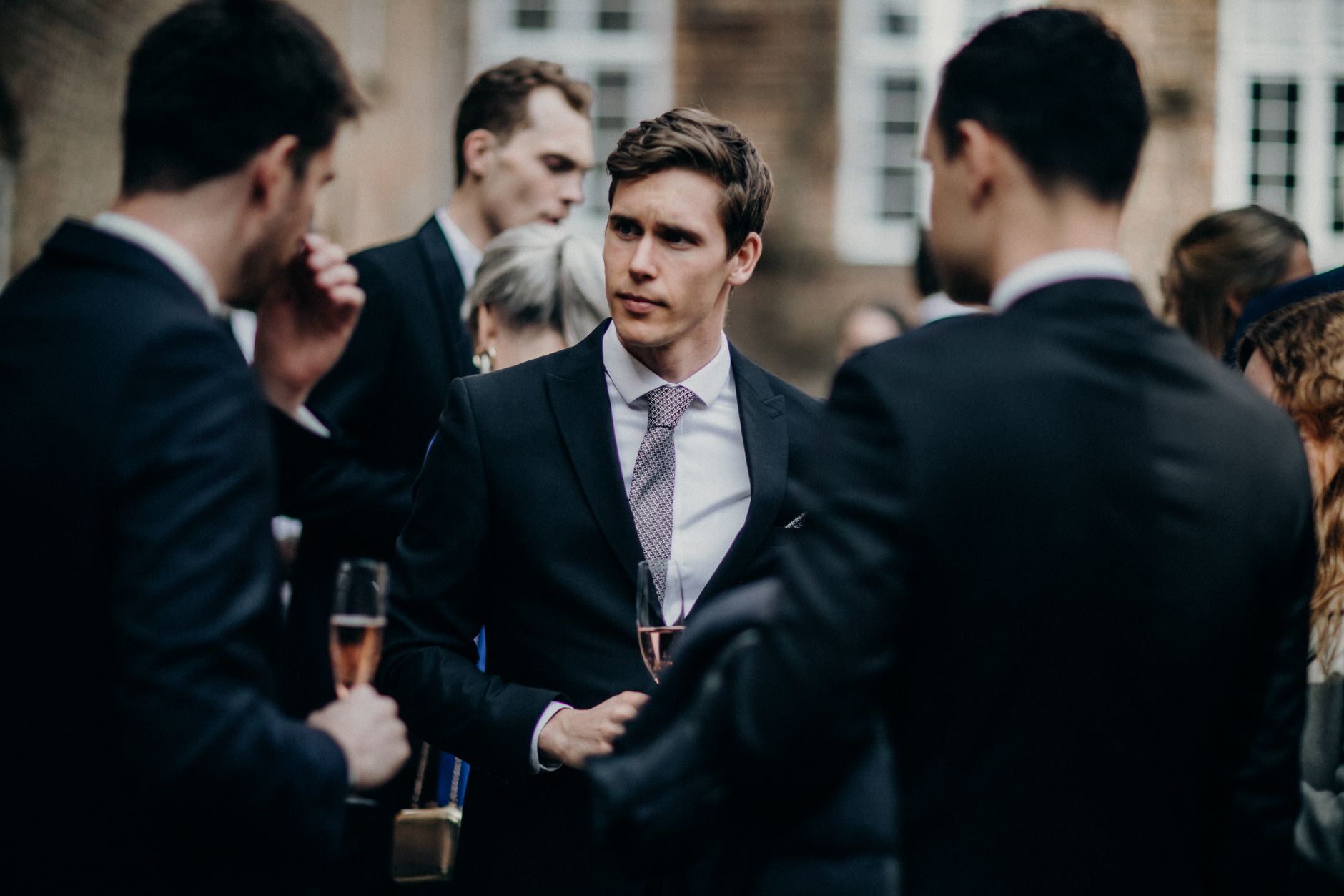 Well-dressed guests engage in conversation at an outdoor wedding reception.