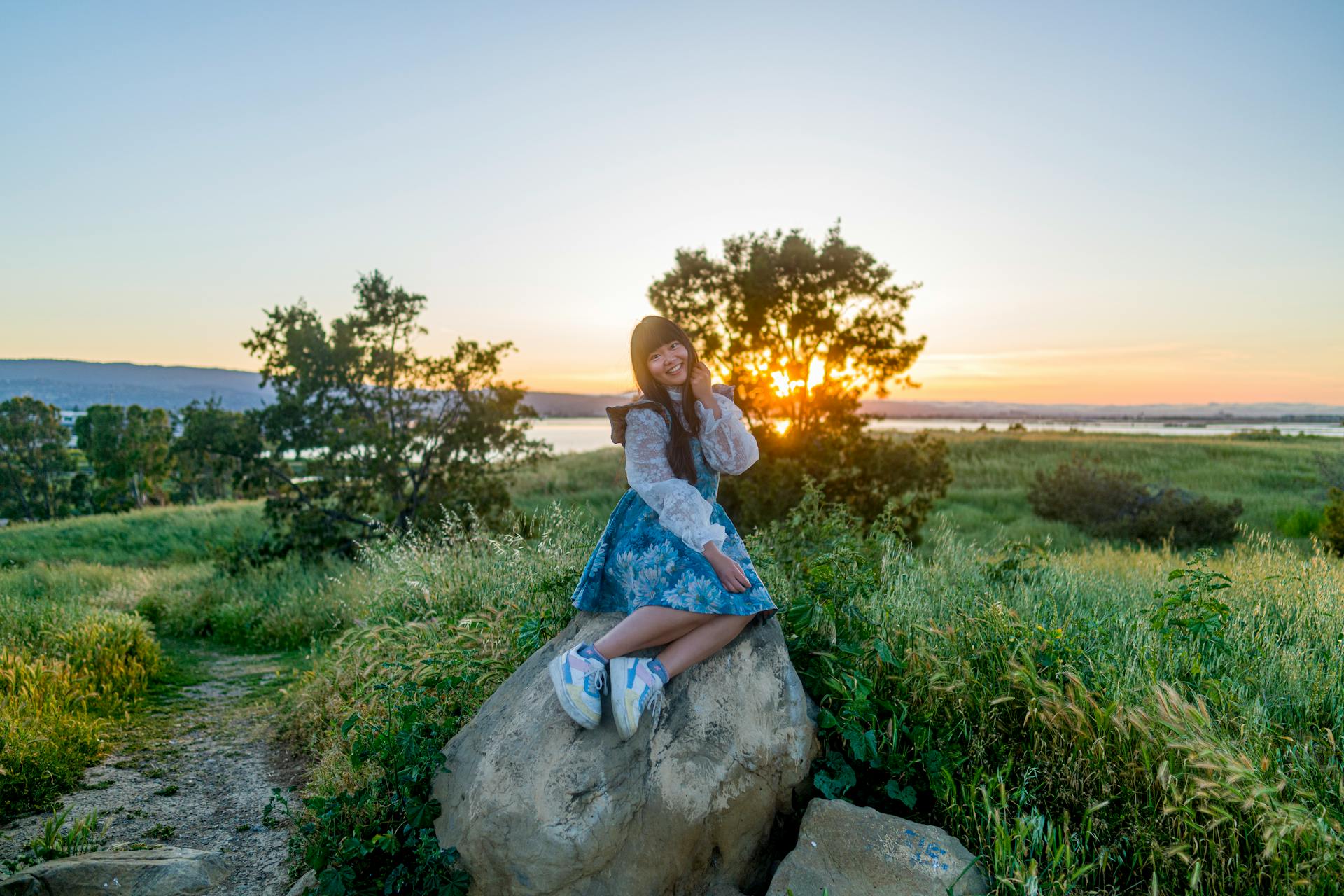 Young woman in a dress sitting on a rock in a Menlo Park field during sunset.