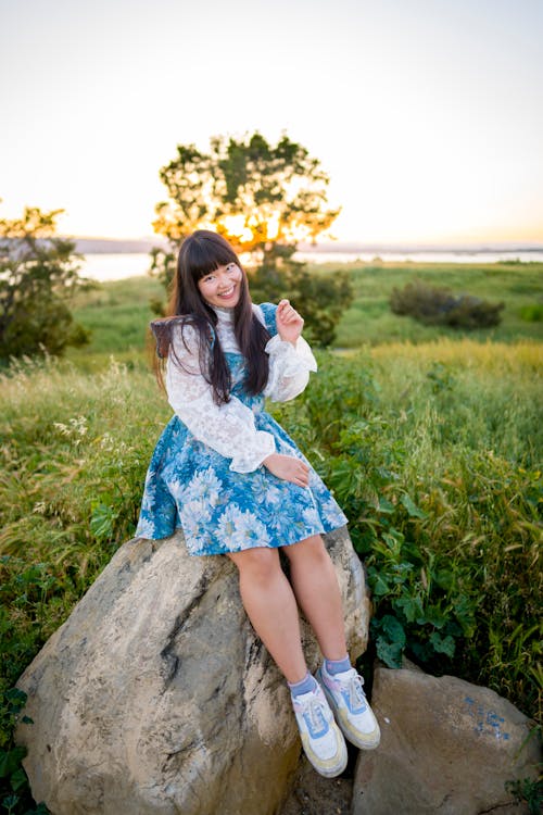 Smiling Woman in Dress Sitting on Rocks on Grassland