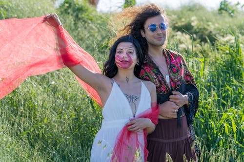 Woman with a Red Handprint on Her Face and Tattoos Walking With Her Boyfriend Dressed as a Hippie in the Meadow