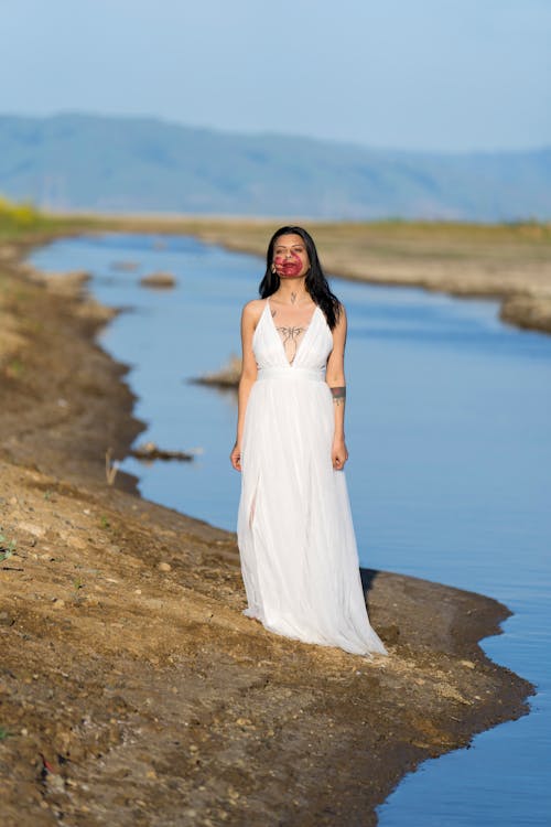 Woman in Wedding Dress and with Painted Face on Riverbank