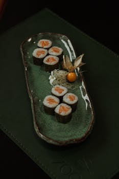 An artistic presentation of sushi with salmon rolls on a green porcelain tray.