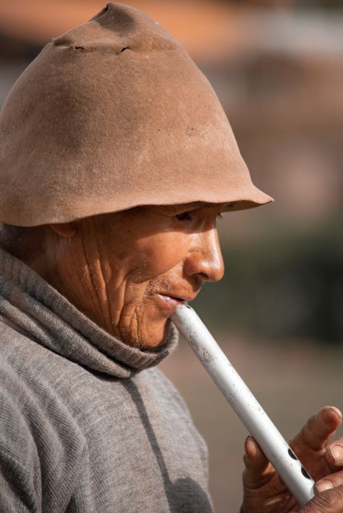Free Elderly Peruvian man playing a flute, wearing a traditional hat outdoors. Stock Photo