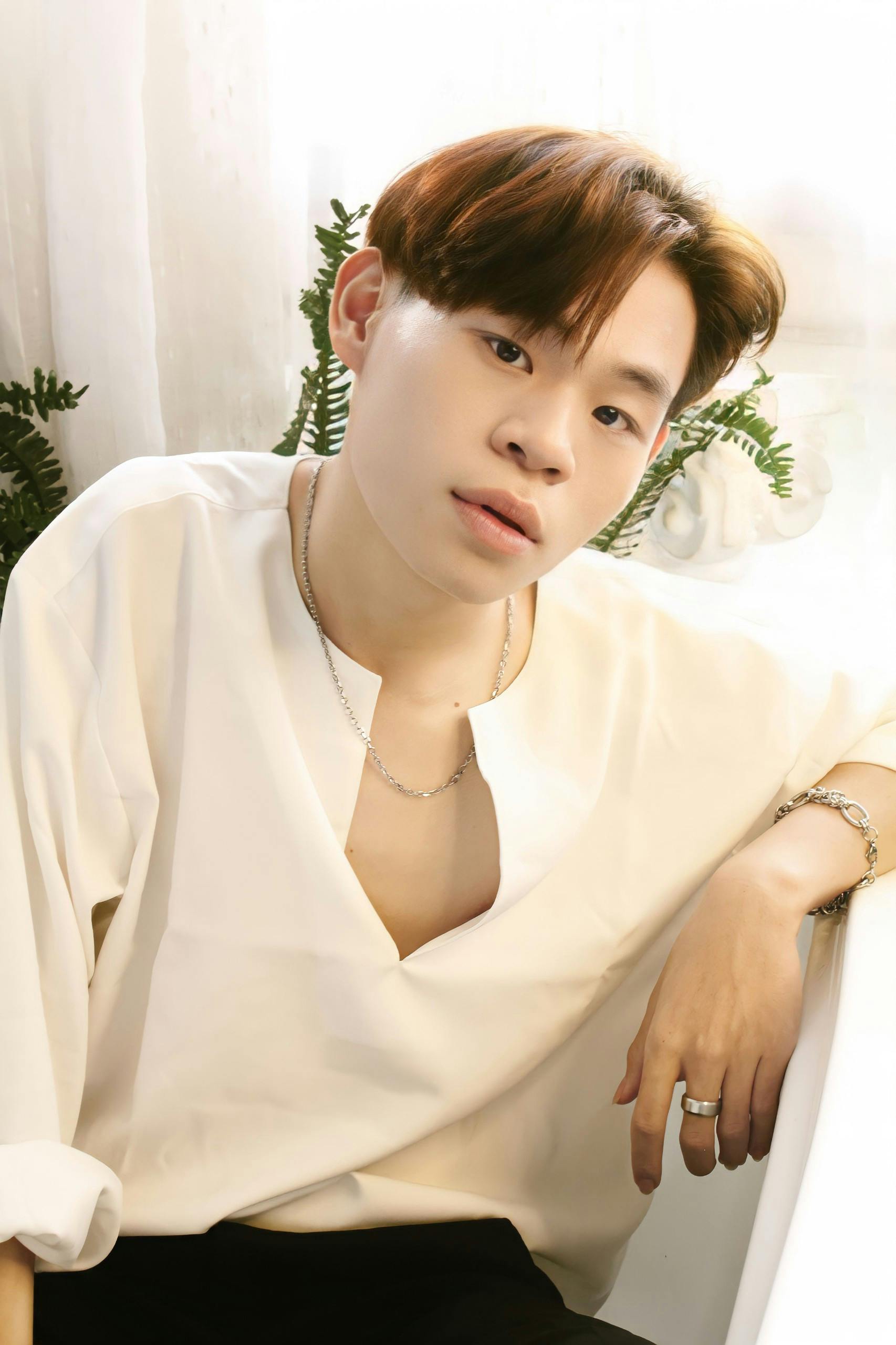 Relaxed portrait of a young man in white shirt with necklaces and rings indoors.