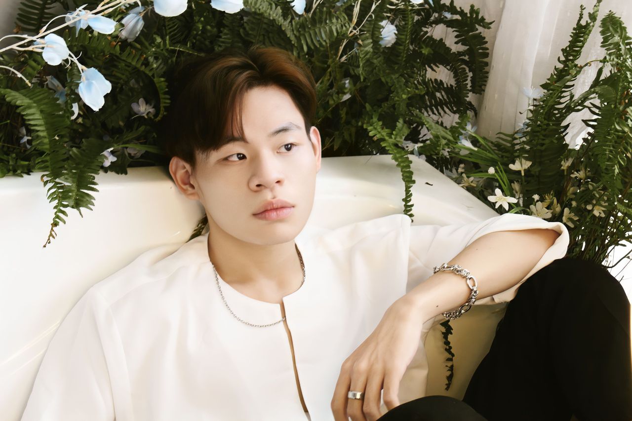 asian man sitting elegantly on a sofa surrounded by lush greenery wear