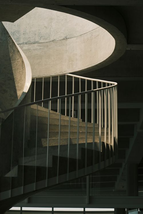 Free Elegant concrete spiral staircase with dramatic shadows and sunlight interplay. Stock Photo