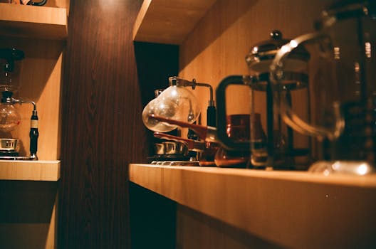 Warm indoors scene of a wooden shelf with various coffee makers and accessories.