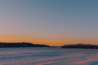日落时分，白雪覆盖的田野和森林地平线构成了一幅宁静的冬季景观