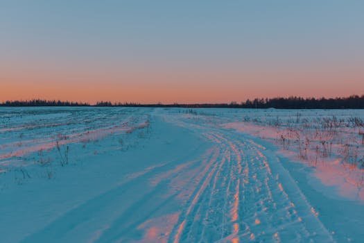 A tranquil snowy field under a vibrant sunset sky, illustrating the calm of a winter evening.