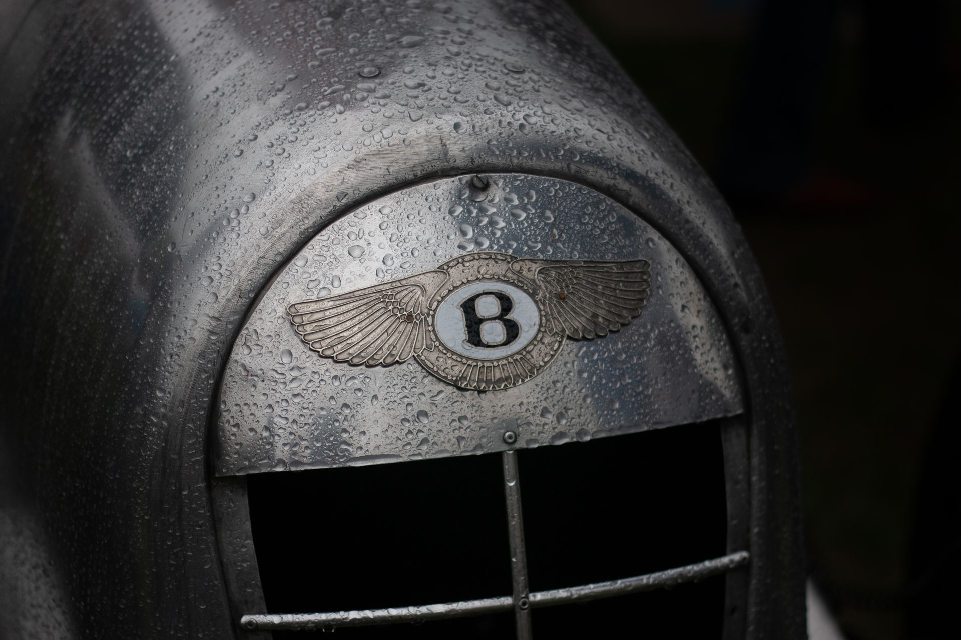 Wet Bentley car emblem on metallic surface, highlighting classic automotive design.
