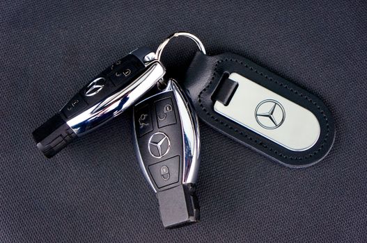Close-up of Mercedes-Benz car keys with a leather keychain on dark fabric background.