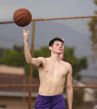 A shirtless young man skillfully spins a basketball on his finger outdoors in Los Angeles.