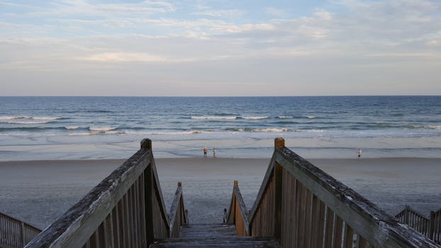 Wooden boardwalk leading to a tranquil beach and ocean view with few people.