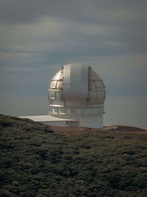 Free A modern observatory dome set against a rugged, natural landscape under a cloudy sky. Stock Photo