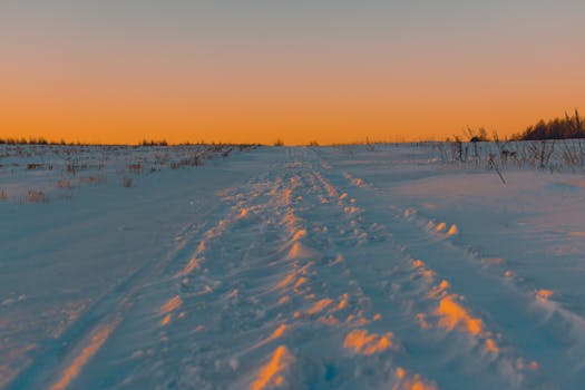 A scenic winter landscape of snow-covered fields under a vibrant sunset sky.