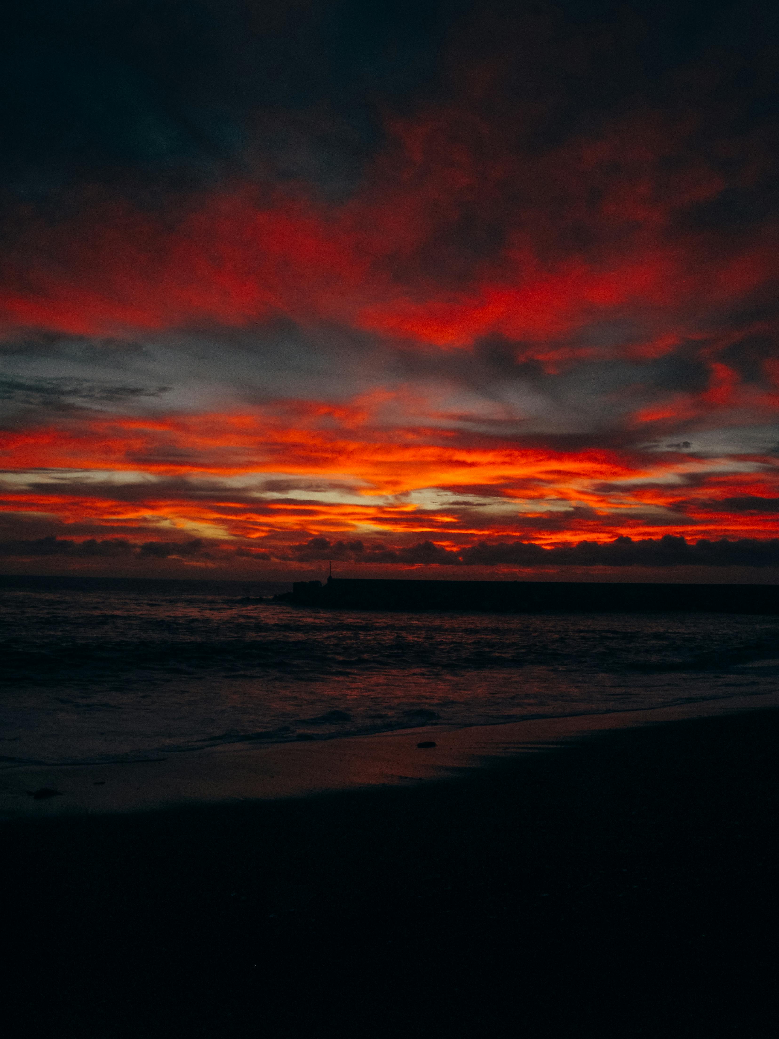宁静的海岸上，天空呈现出鲜艳的红色和橙色，日落景色令人惊叹