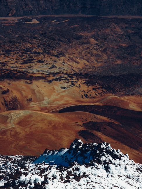A breathtaking aerial view of snow-capped mountains set against a warm, earthy desert landscape.