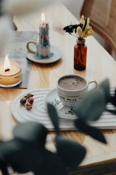 A serene coffee moment with candles and flowers on a wooden table.