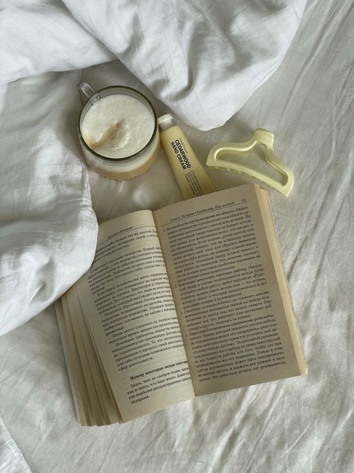 Free A relaxing scene featuring an open book, cappuccino, and hair clip on a bed. Stock Photo