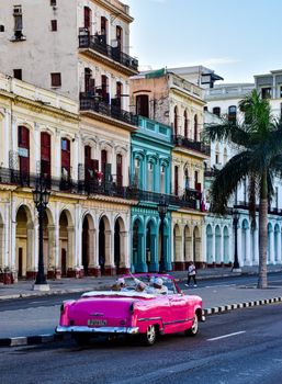 Classic pink cabriolet cruising on a colorful street in Havana, Cuba.