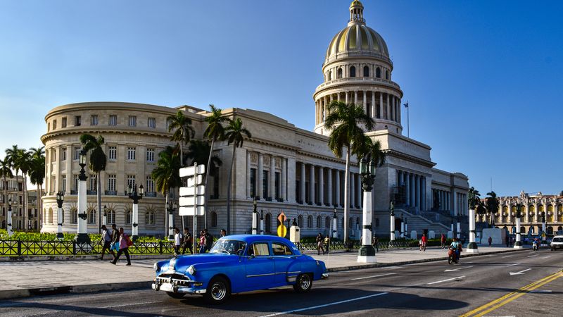 Classic blue car on Havana street with iconic Capitolio building in background.
