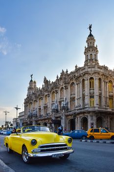 A vibrant yellow classic car parked in front of the iconic Grand Theater in Havana, Cuba.
