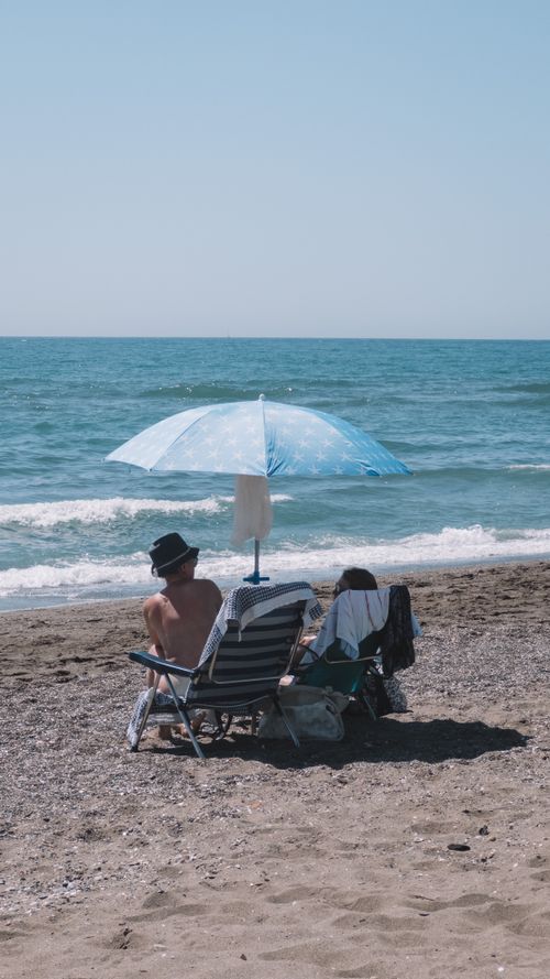 Free Couple enjoying a serene beach day under an umbrella in Málaga, Spain. Stock Photo