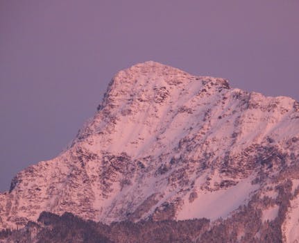 A breathtaking view of a snow-covered mountain peak bathed in pink hues at sunset.