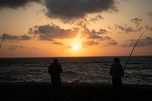 Silhouetted fishermen casting lines against a vibrant sunset in Alexandria, Egypt.