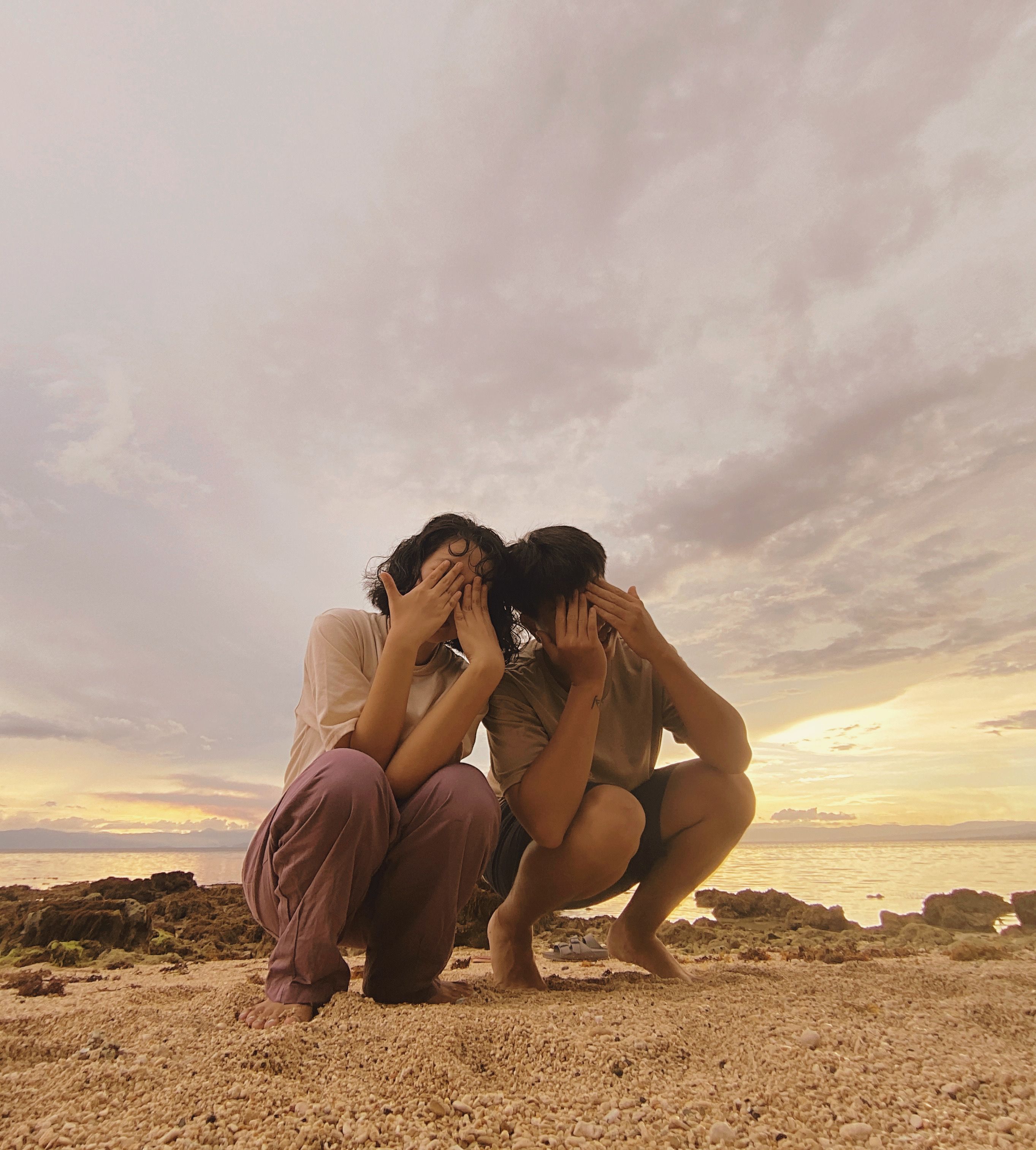 Two friends covering their faces while enjoying a beachfront sunset in Cebu, Philippines.