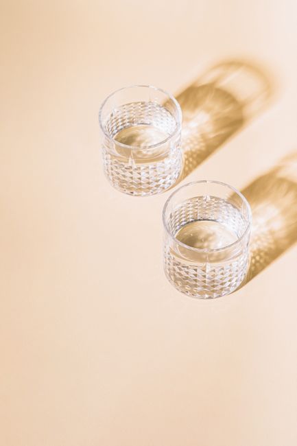 Two clear glasses casting intricate shadows on a beige surface, showcasing minimalist elegance.
