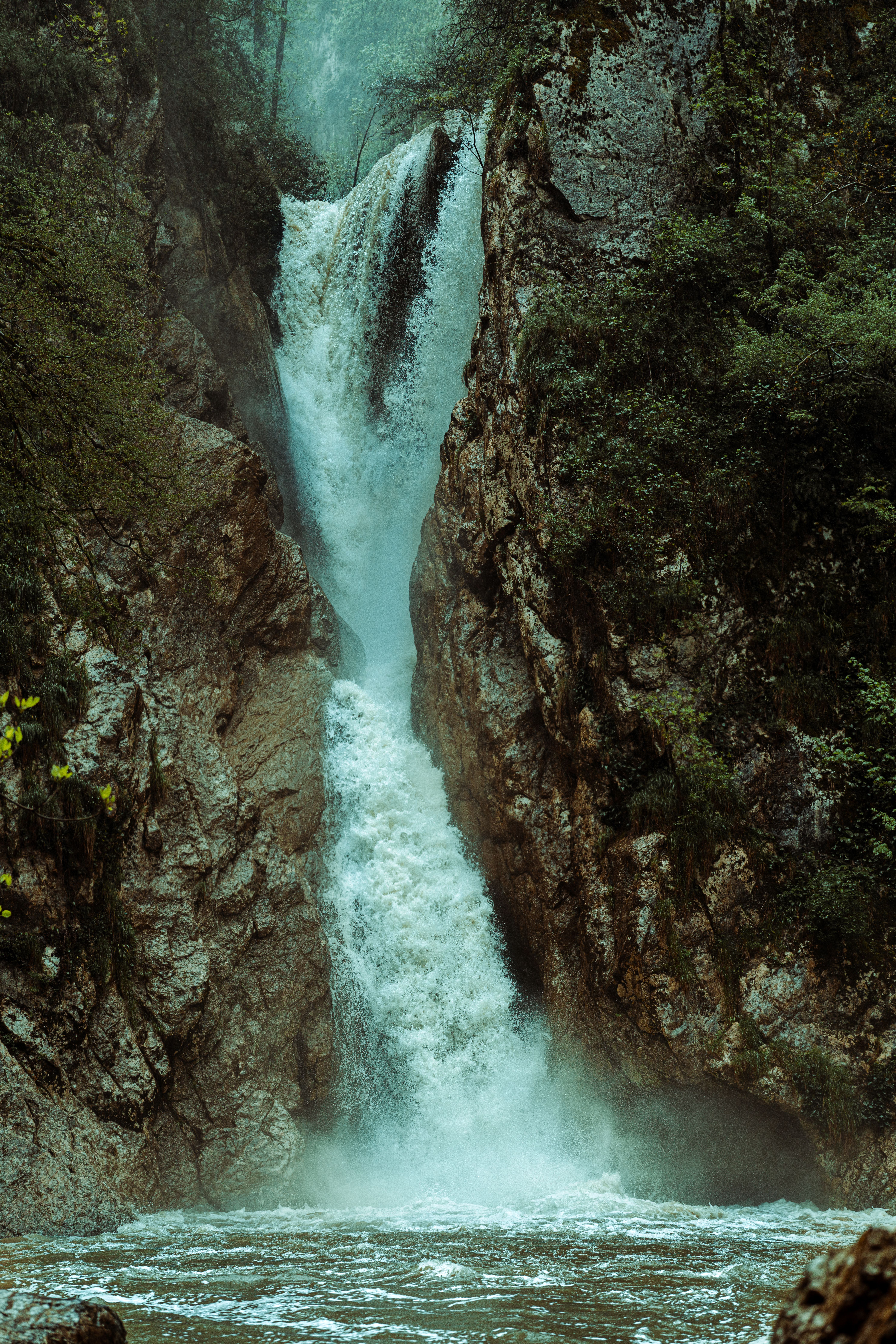 Vertical waterfall cascading through rocky cliffs surrounded by dense forest.