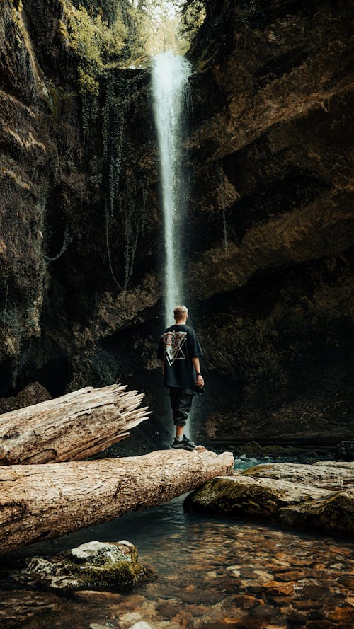 Man Standing on a Tree Log by the Waterfall