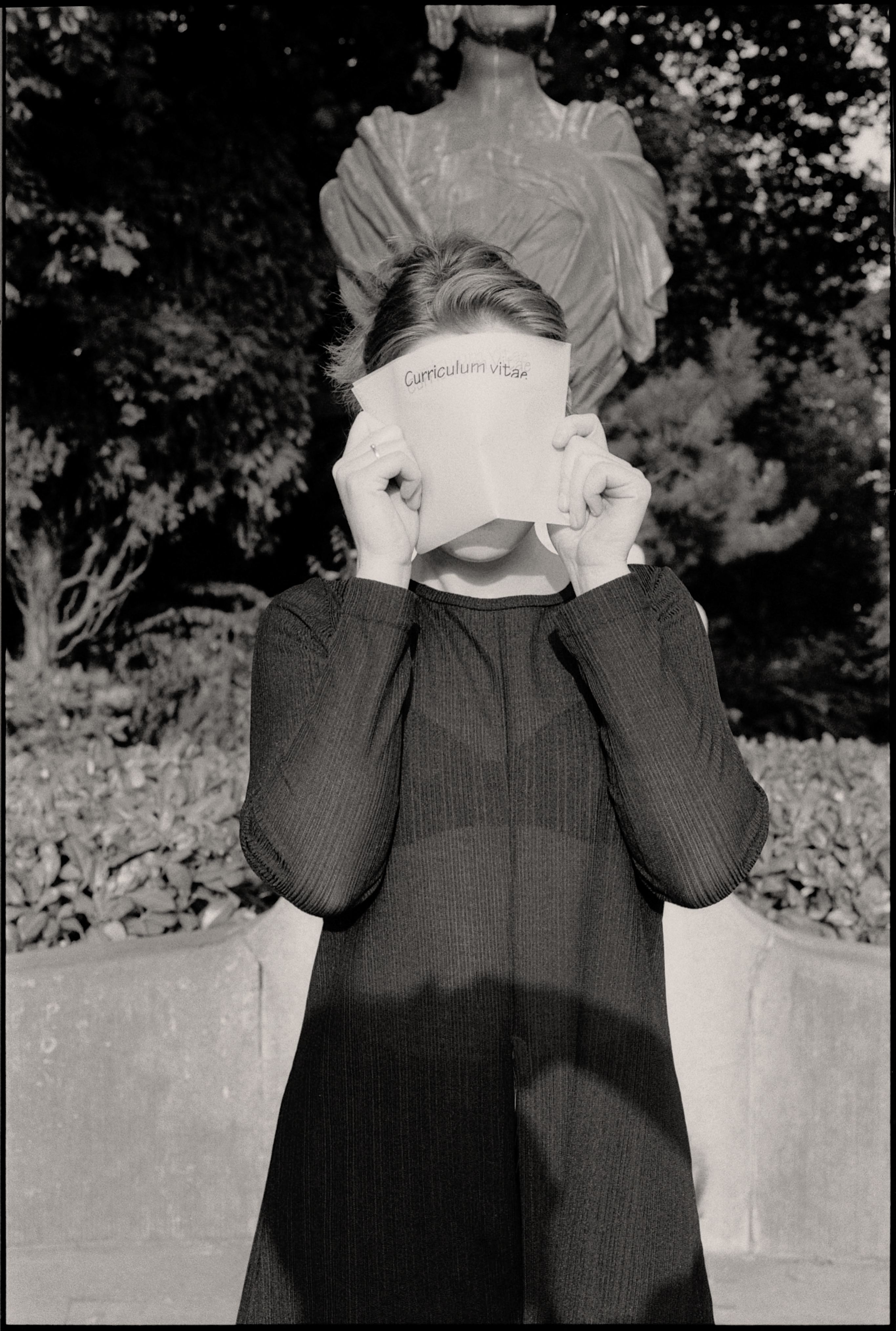 Woman Covering Face with Curriculum Vitae against Sculpture