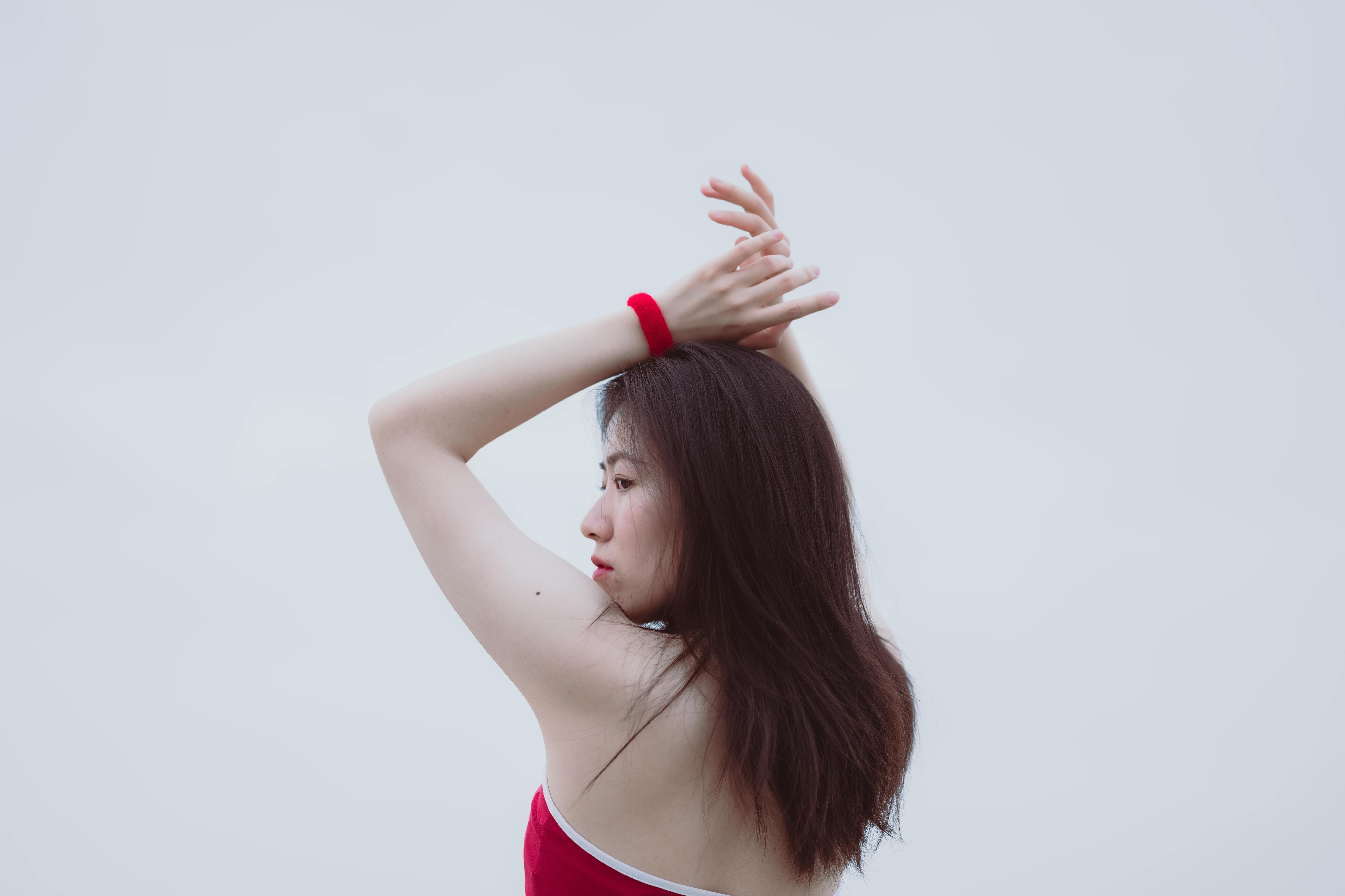 Artistic portrait of an Asian woman with arms raised, wearing red top.