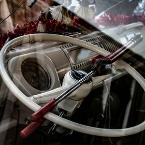 Bar-type steering wheel lock with red handles hooked across the cream steering wheel of a classic camper van, seen through the window