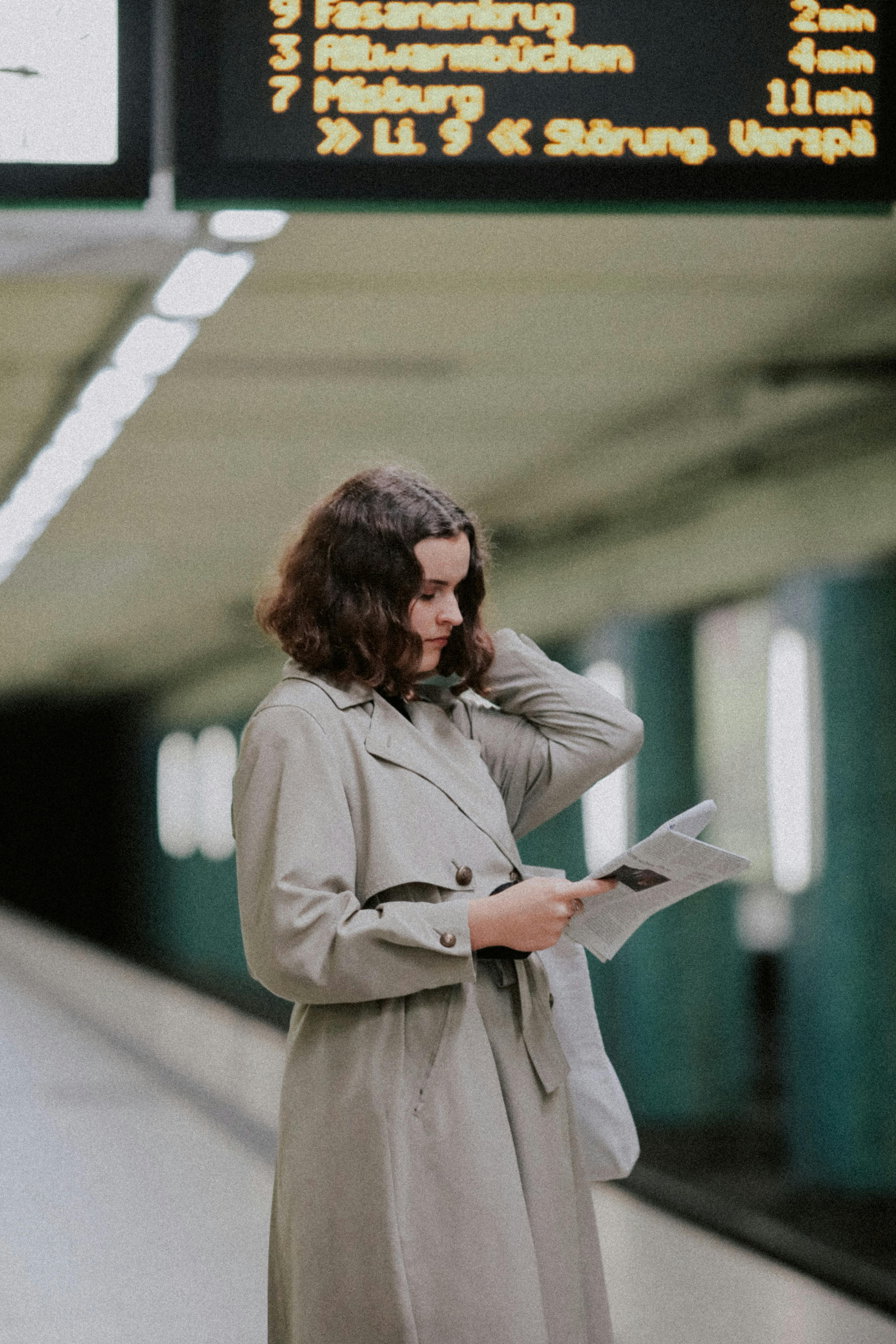 A woman in a trench coat reads a newspaper at a metro station in Hanover, Germany.
