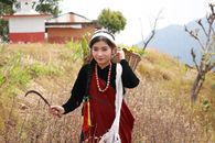 Portrait of a Nepalese woman in traditional attire carrying a basket in a rural landscape.